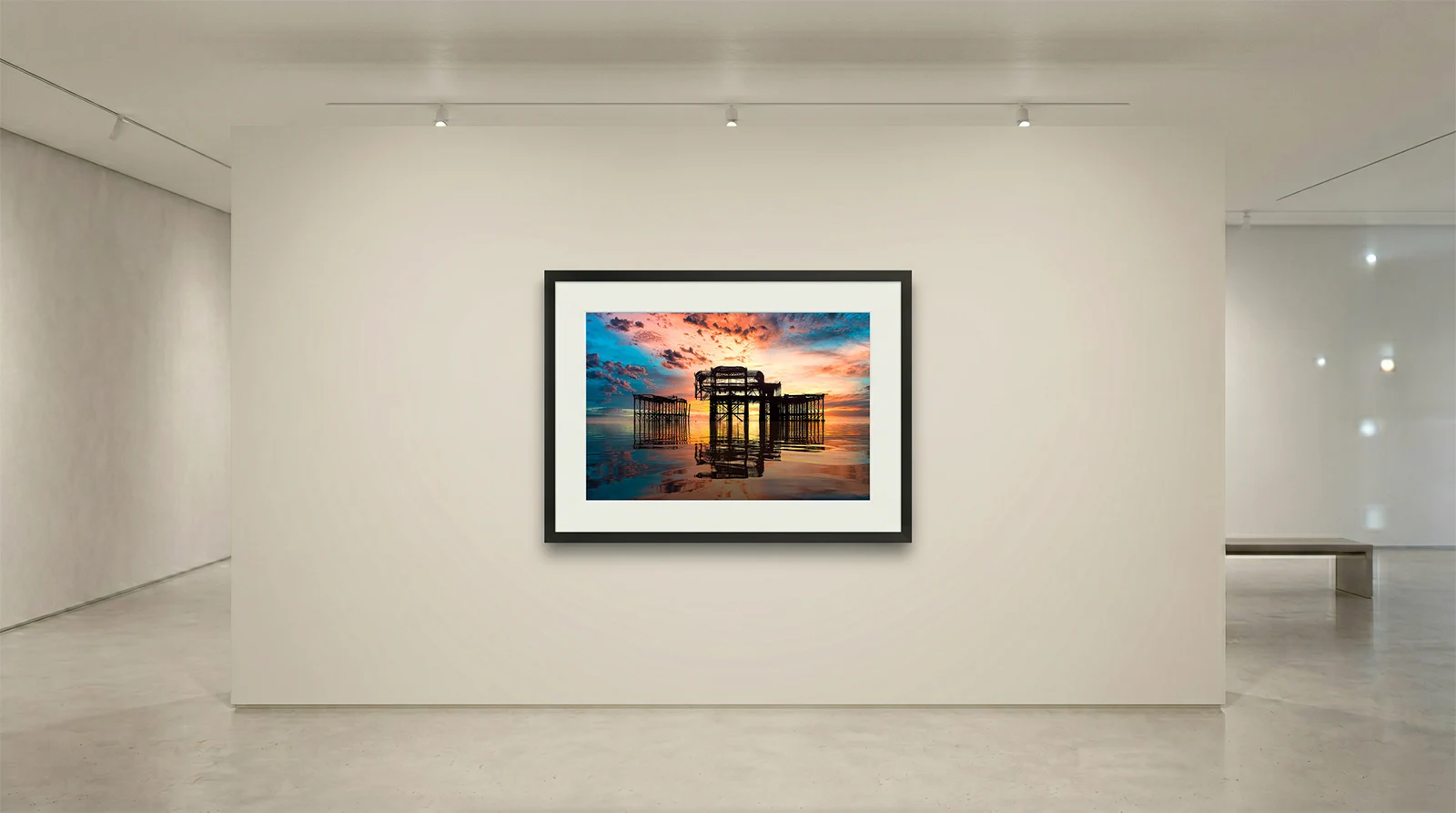 Fine art print of the West Pier in Brighton by Brian Roe, framed in black on a white wall inside a minimalist modern art gallery setup.