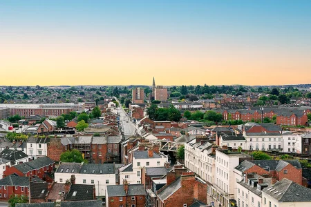 A high-angle view looking over the brick rooftops, urban street layout, and residential chimneys of South Leamington Spa at sunrise.