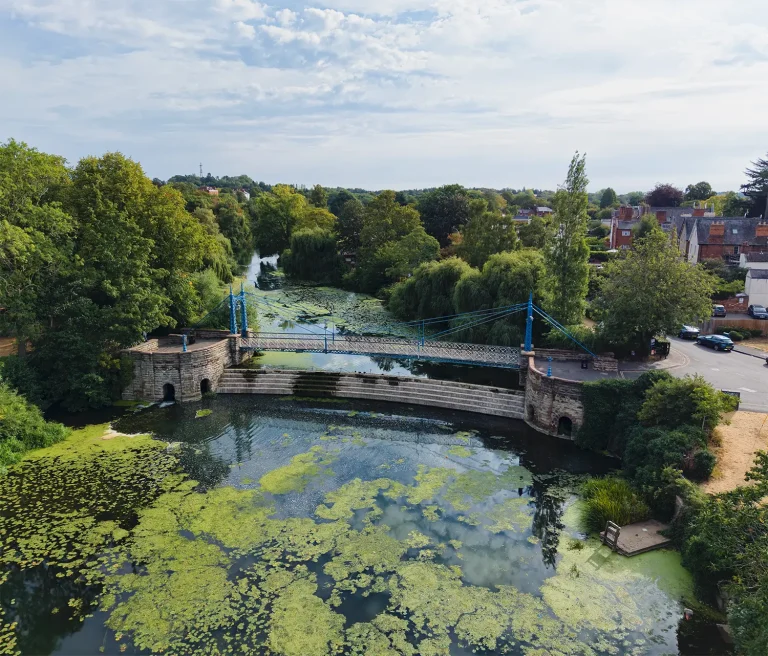 A Love Letter Written in Blue Iron – The iconic blue Mill Bridge and weir on the River Leam Aerial view of the blue iron Mill Bridge and stepped weir on the River Leam in Royal